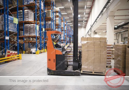 Industrial worker in protective uniform operating forklift in big warehouse distribution center. Industrial worker in protective uniform operating forklift in big warehouse distribution center.